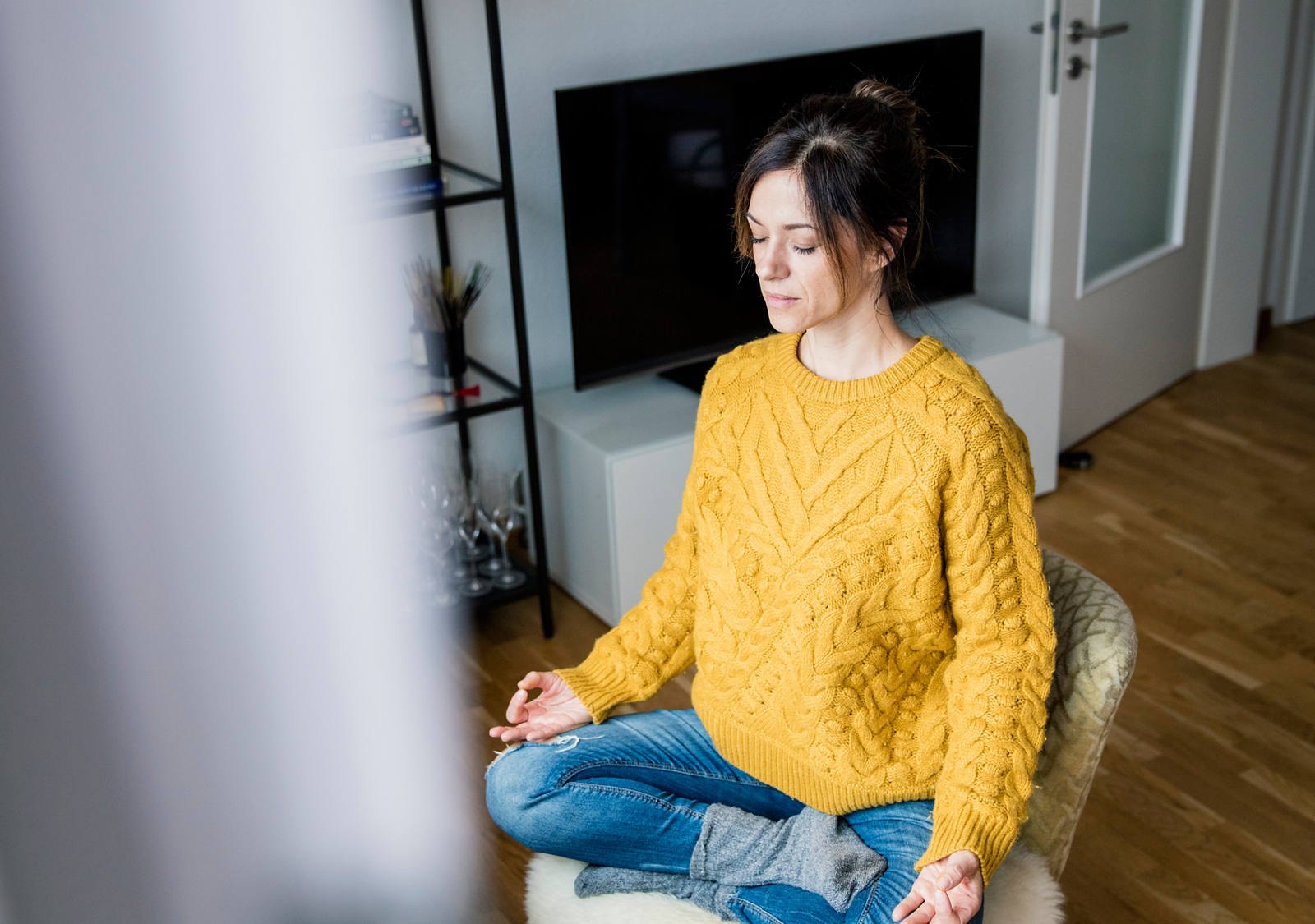 A woman sits in a tailor’s seat in the living room, meditating.