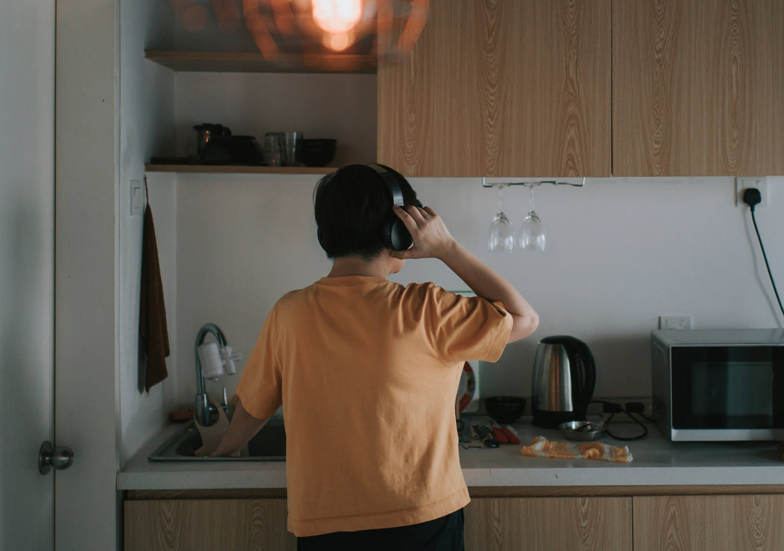 Ein Mann trägt Kopfhörer und steht in seiner Küche vor dem Spühlbecken.