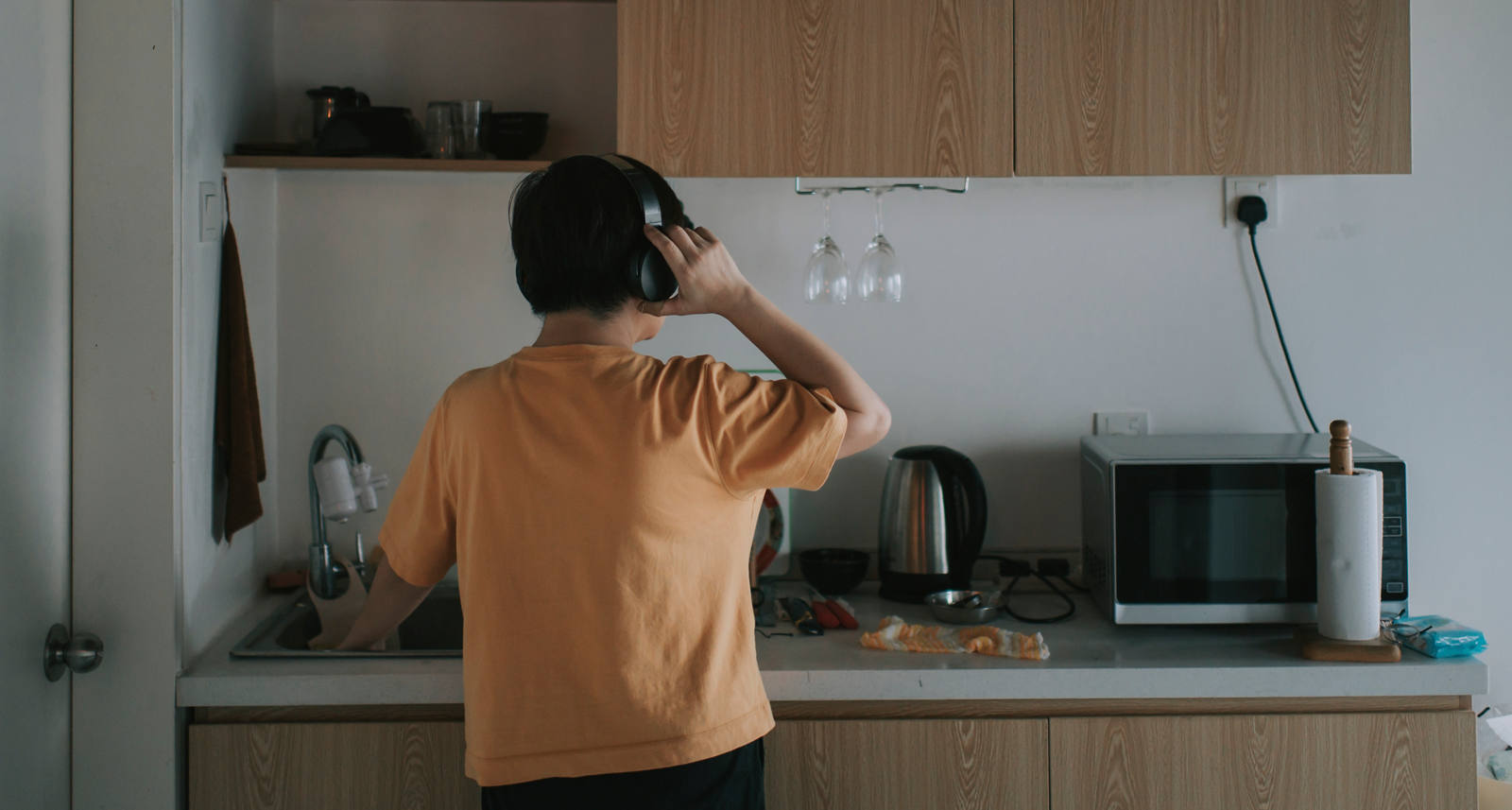 Un homme porte des écouteurs et se tient devant l’évier dans sa cuisine.