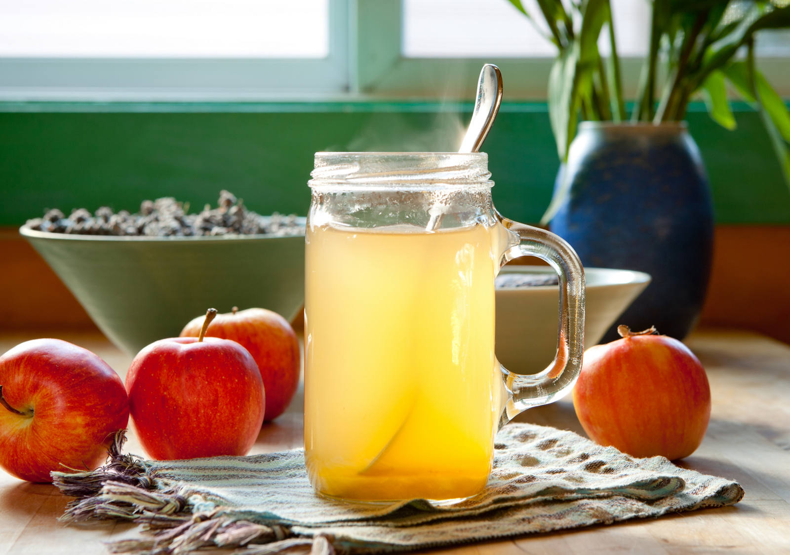 A large glass of warm apple cider vinegar stands on a table next to fresh apples.