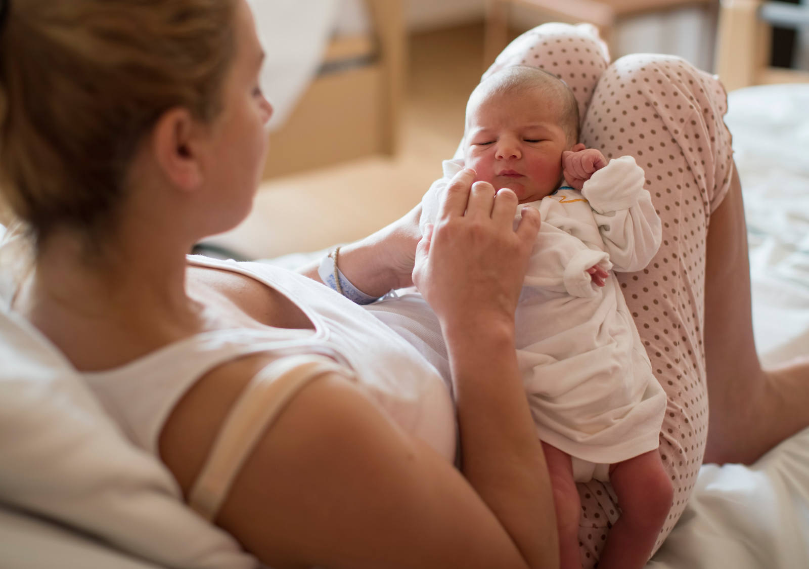 Junge Mutter liegt mit ihrem Neugeborenen im Bett