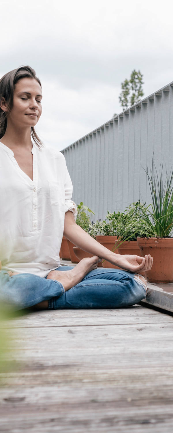 Frau meditiert im Schneidersitz auf dem Balkon