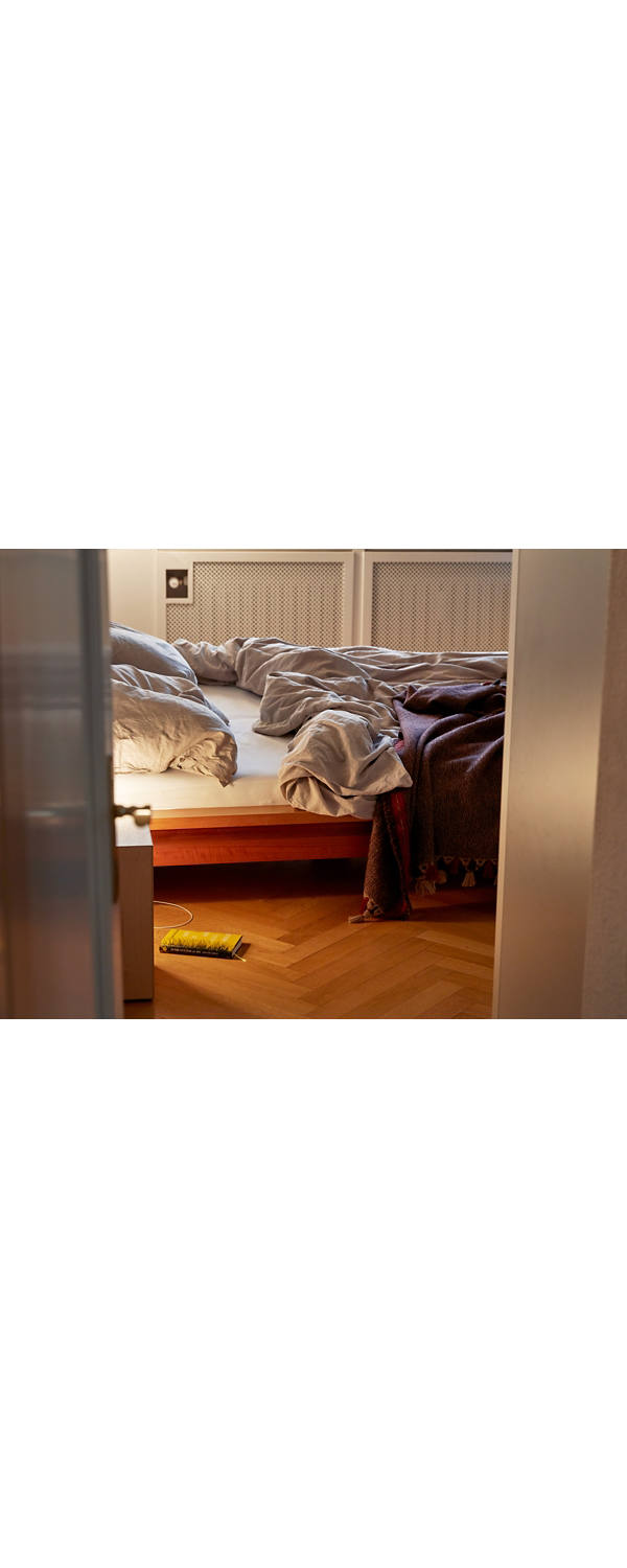 Ein ungemachtes Bett und eine brennende Nachttischlampe.