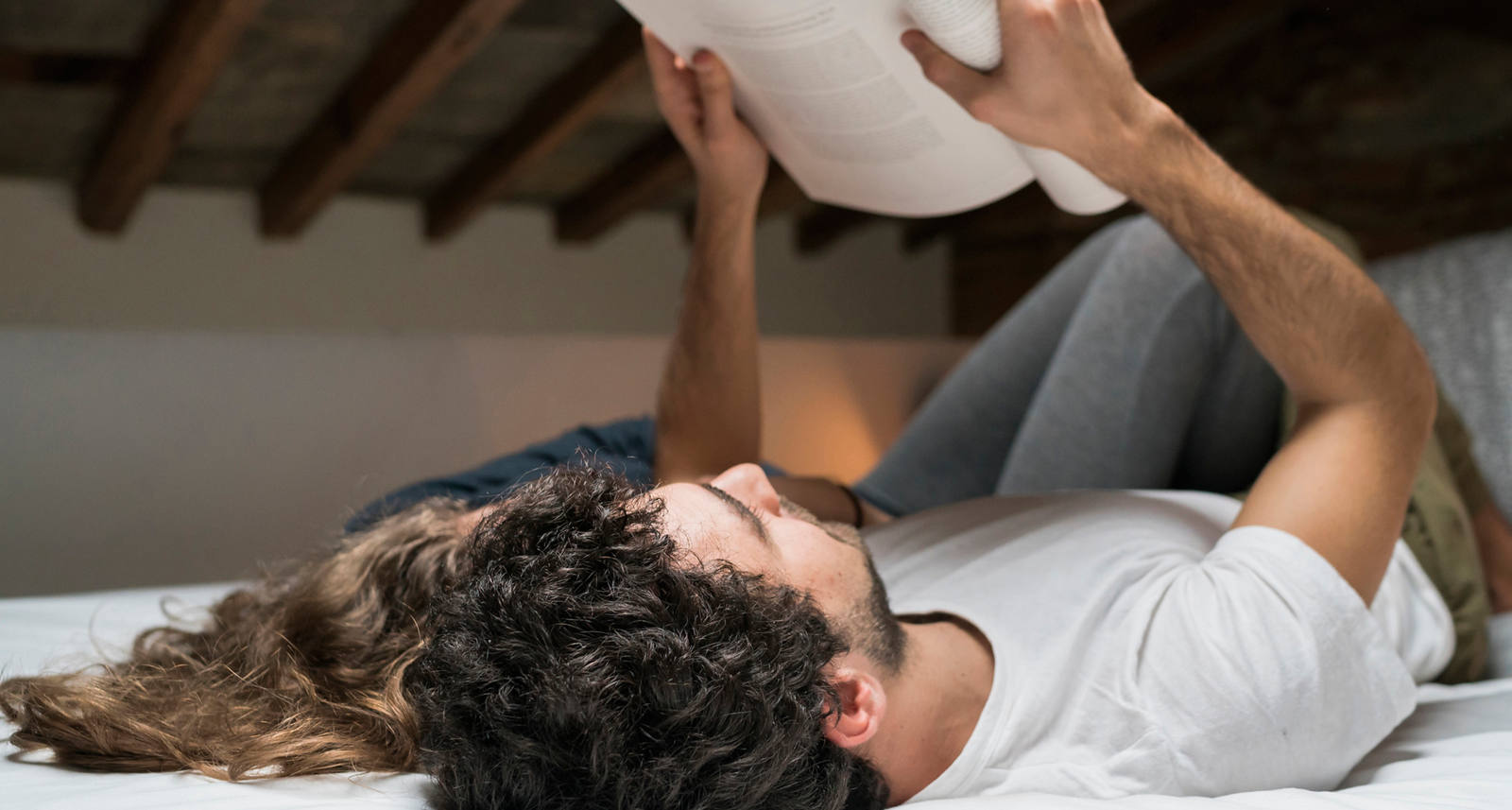 Ein Paar liegt auf dem Bett und liest in einem Heft.