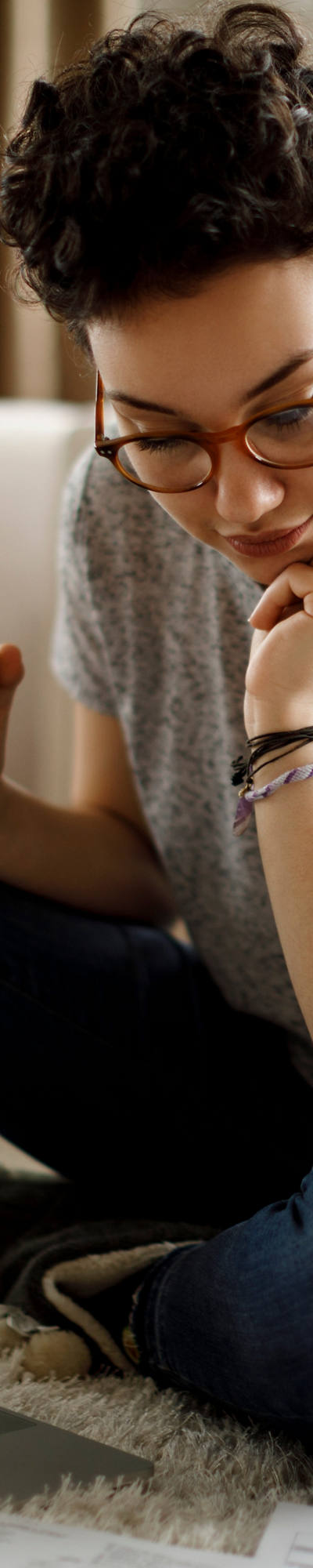 Frau sitzt vor Sofa auf Teppich mit Laptop zu Ihren Füssen und studiert Dokumente