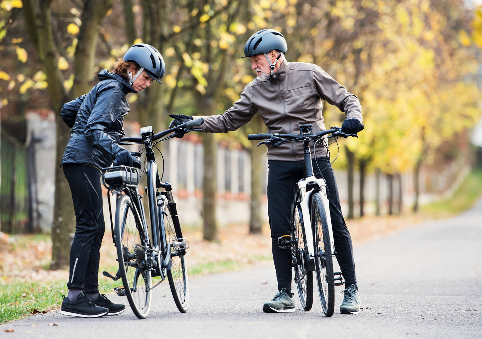 An older couple is riding an e-bike in the park and they are wearing a helmet.