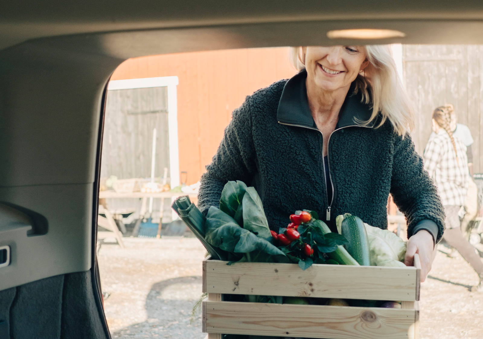 Frau trägt eine Holzkiste mit Marktgemüse zum Auto.