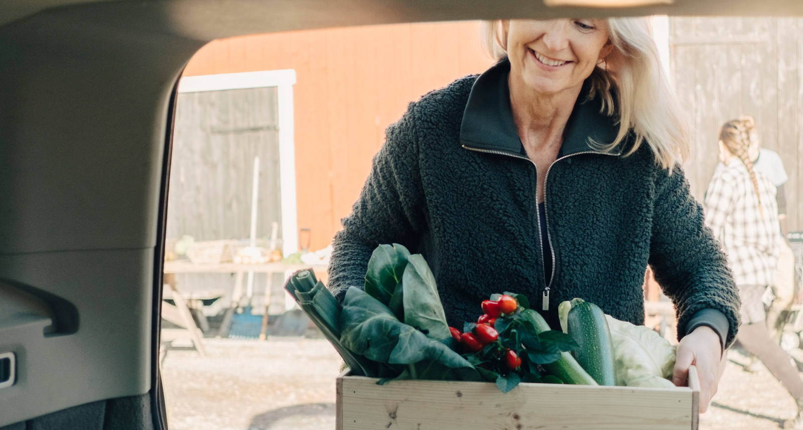 Frau trägt eine Holzkiste mit Marktgemüse zum Auto.