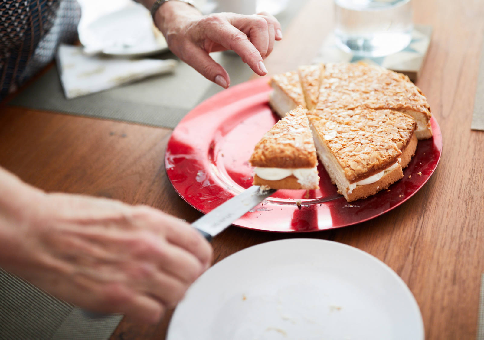 Eine Frau hat den Kuchen in Stücke geschnitten und richtet die Kuchenstücke auf Dessert-Teller an.
