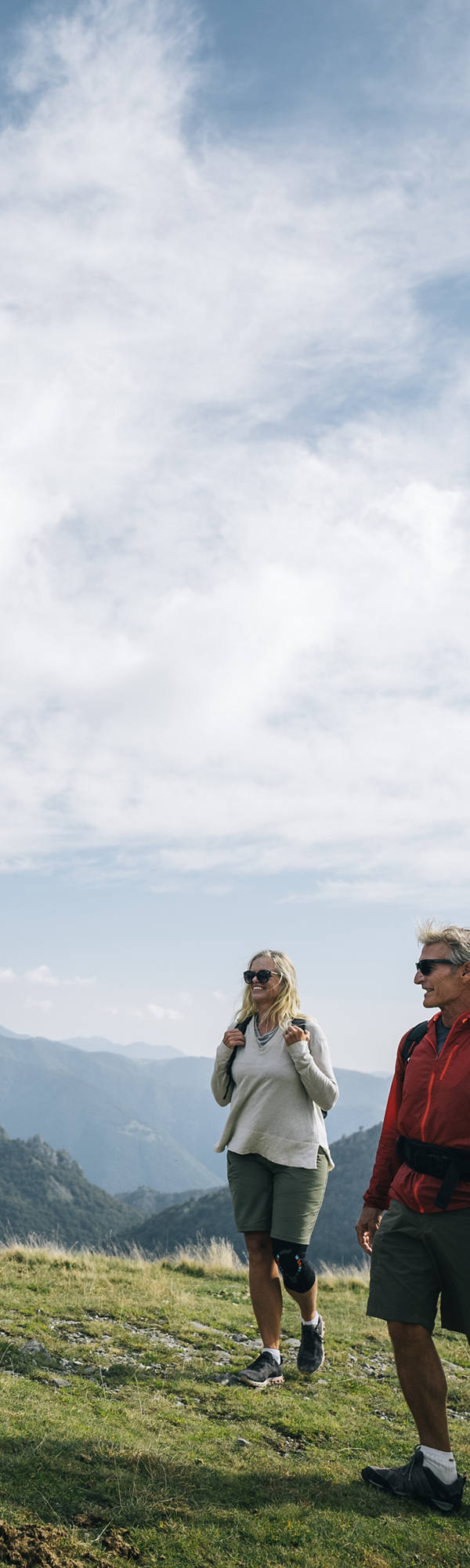 Eine Familie wandert bei schönem Wetter in den Bergen über eine Wiese und hat Spass.