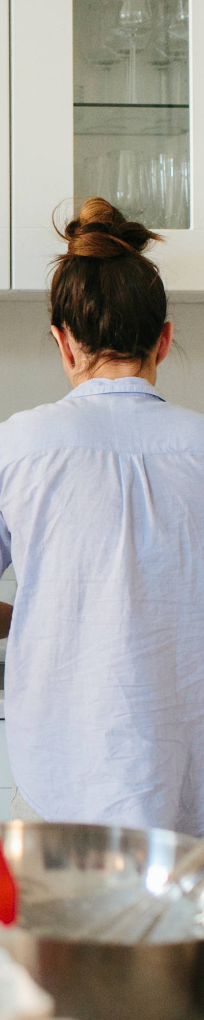 Junge Familie steht gemeinsam in der Küche. Der Vater hält ein Neugeborenes und liest die Zeitung.