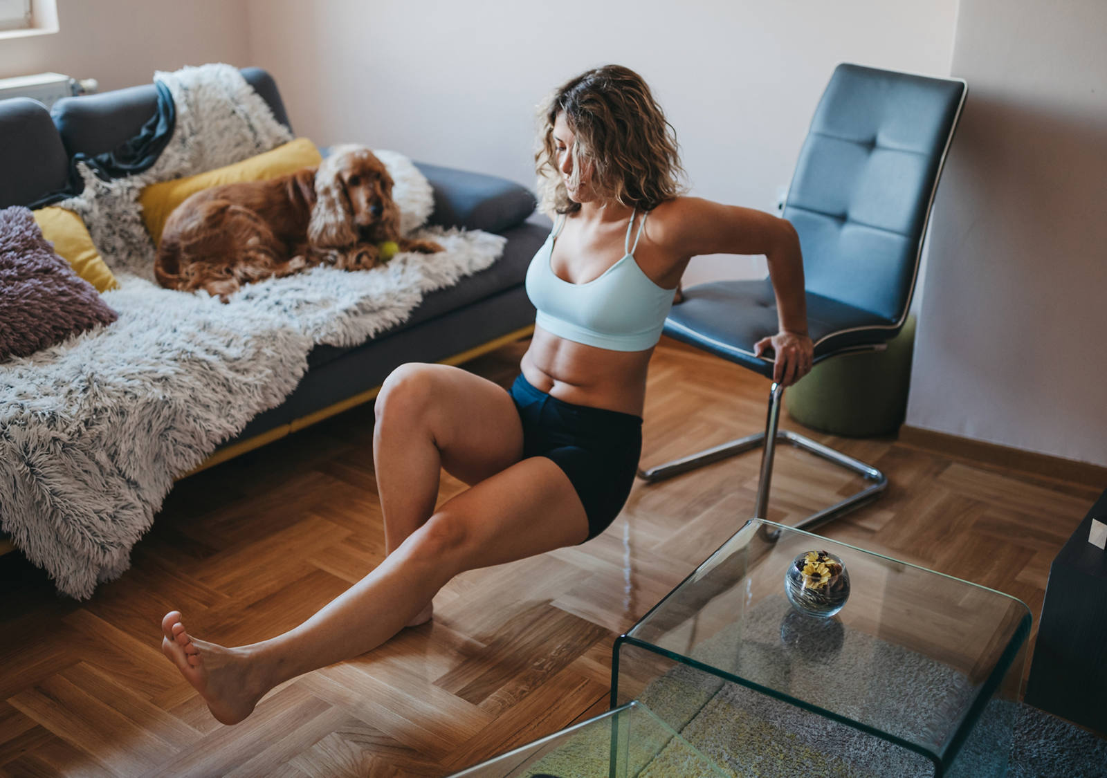 Frau macht Armbeugen-Training zu Hause in Wohnzimmer mit Hilfe eines Stuhls.