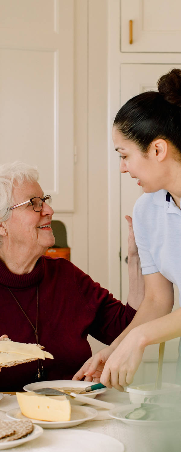 In the kitchen, an old woman receives support from a nurse.