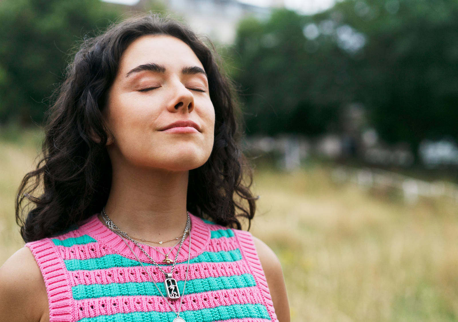 A woman stands on a meadow with her eyes closed and takes a deep breath.