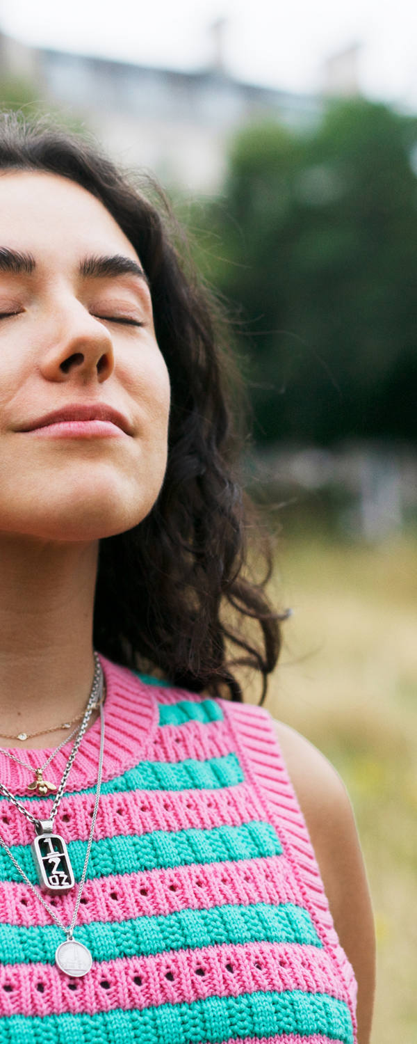 Une femme se tient dans une prairie les yeux fermés et respire profondément.