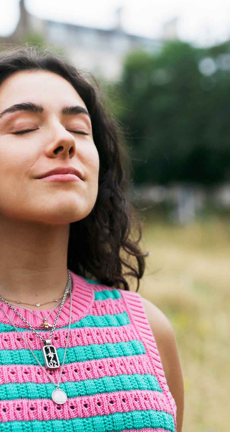 Une femme se tient dans une prairie les yeux fermés et respire profondément.
