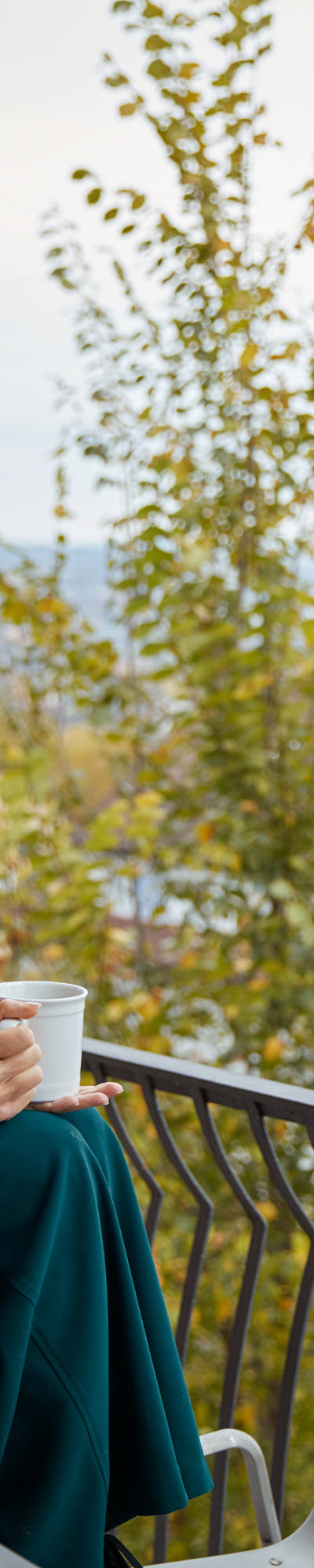 Femme assise sur la table sur son balcon avec une tasse à la main