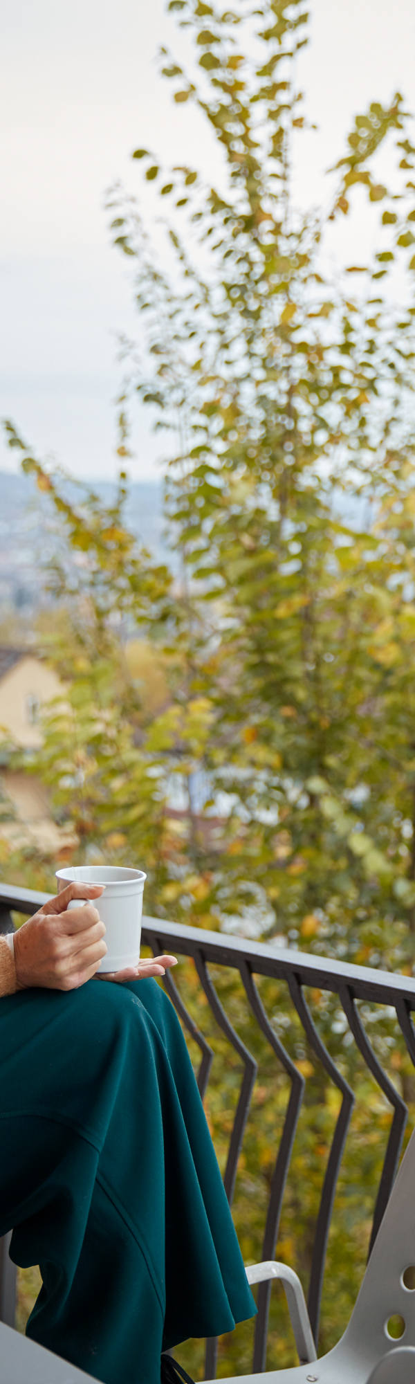 Woman sitting on table on her balcony with cup in hand