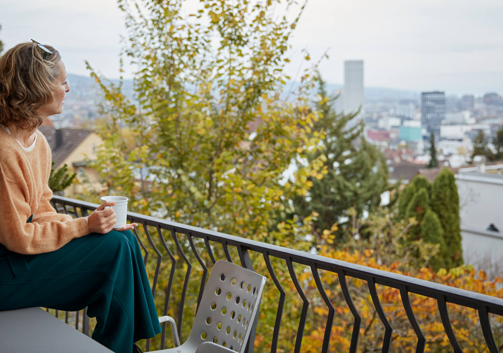 Frau sitzt auf Tisch auf ihrem Balkon mit Tasse in der Hand