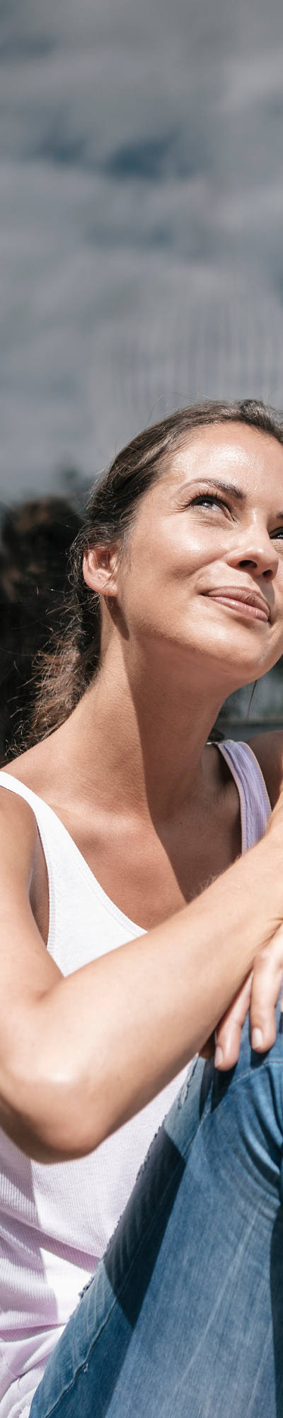 Eine Frau sitzt auf dem Balkon-Boden mit einer Tasse in der Hand und geniesst die Sonnenstrahlen.