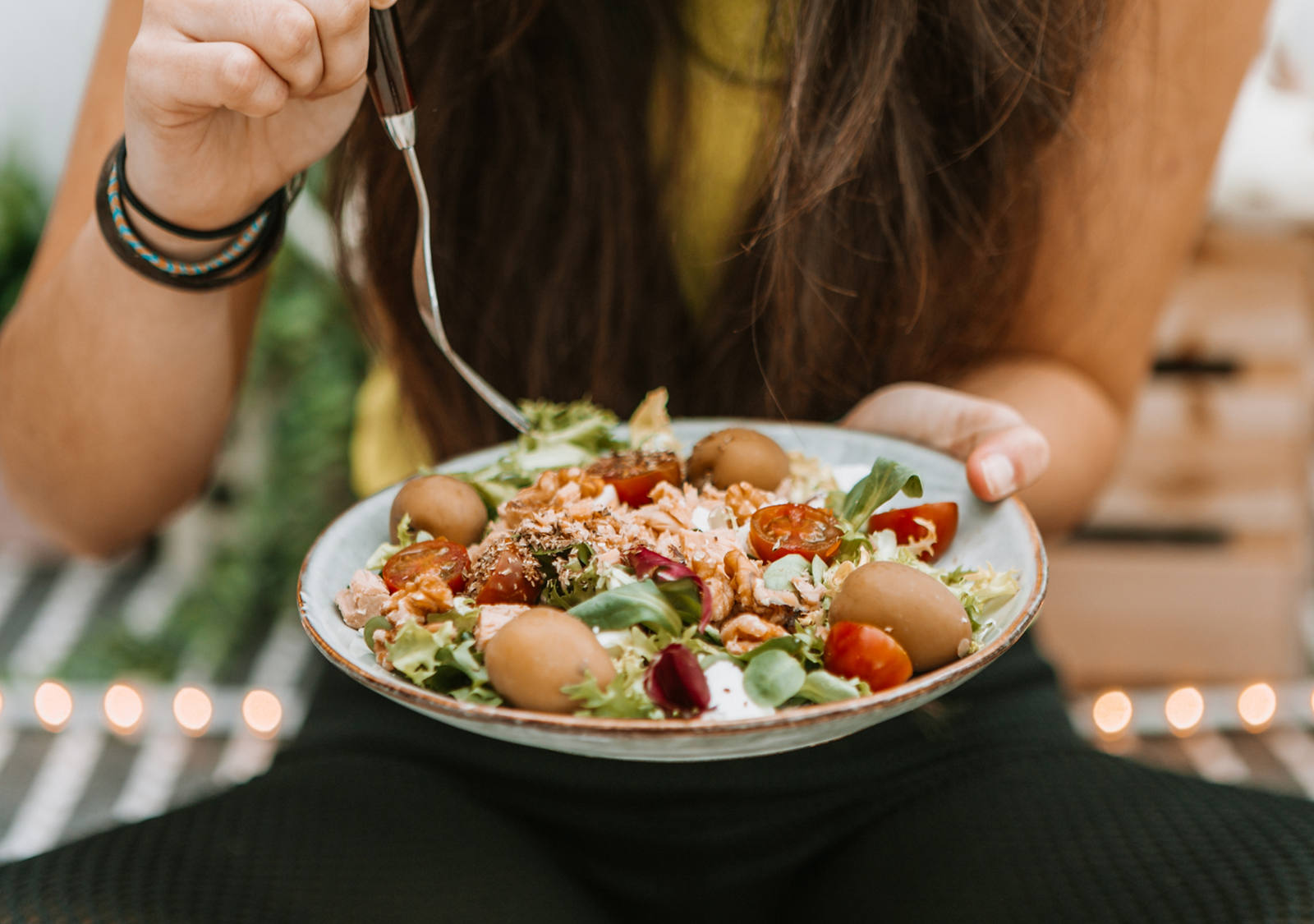 Die Frau sitzt im Schneidersitz am Boden und isst einen ballaststoffreichen Salat-Teller mit der Kabel.
