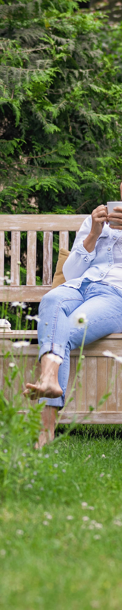 Woman sitting on a wooden bench in the garden enjoying a drink.
