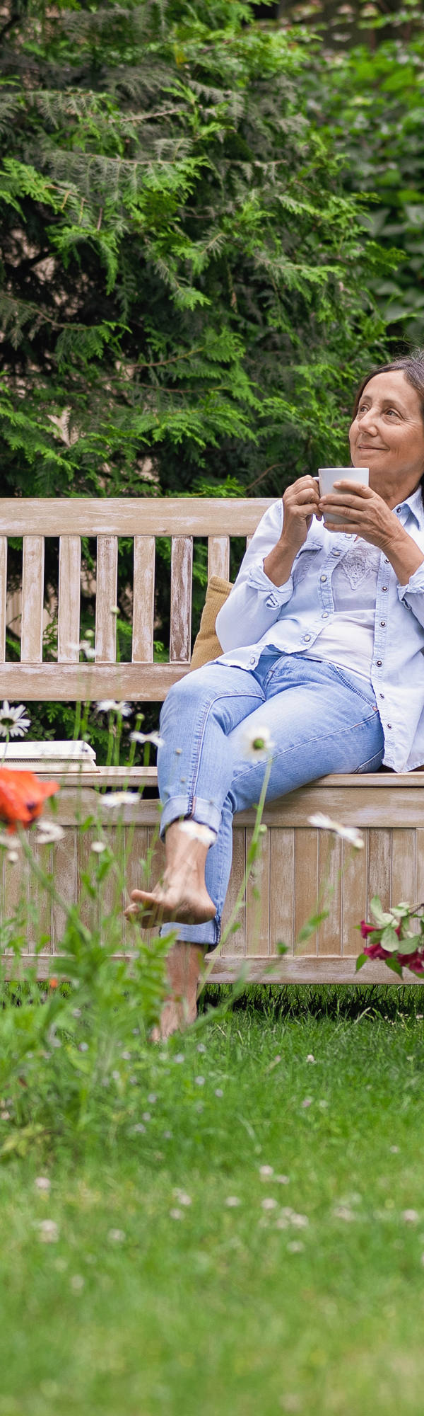 Une femme est assise sur un banc en bois dans le jardin et profite d’une boisson.