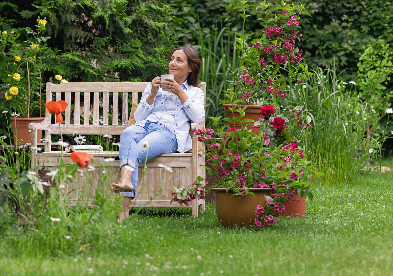 Woman sitting on a wooden bench in the garden enjoying a drink.
