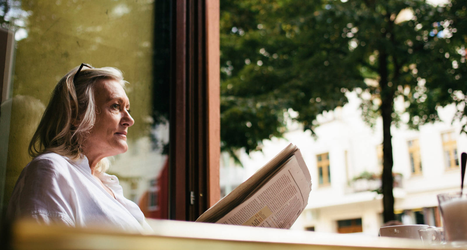 Una donna anziana legge il giornale con la finestra aperta