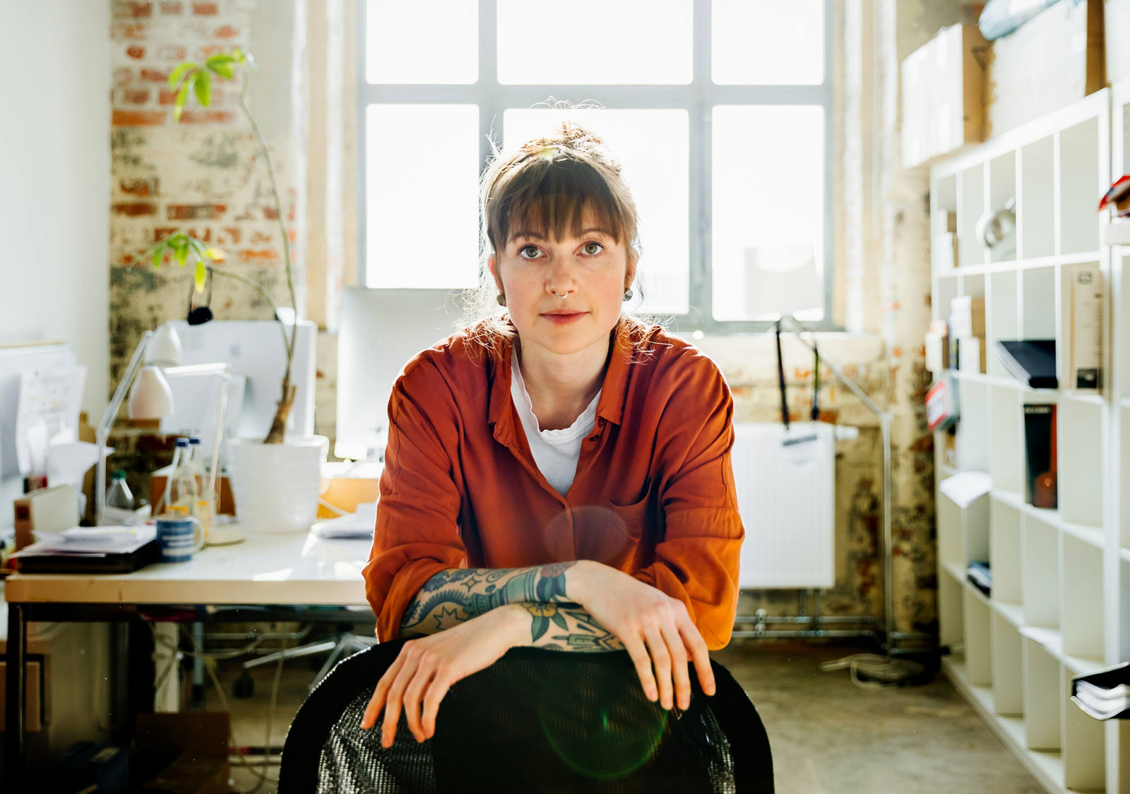 Une jeune femme est assise dans son bureau et regarde l’objectif avec assurance.