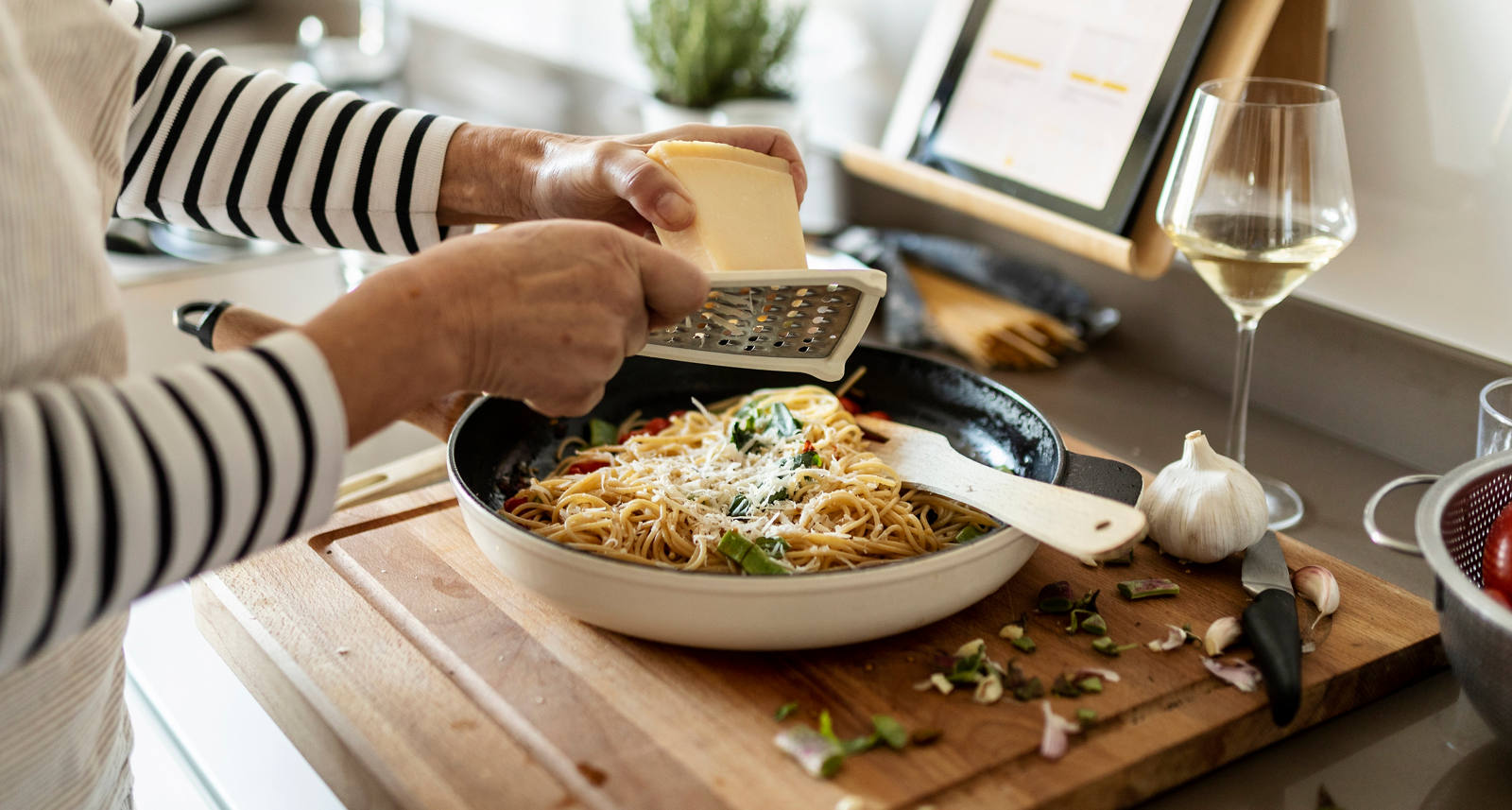 Eine Frau bereitet sich in der Küche ihre Malzeit zu und raffelt Käse über das Gericht.