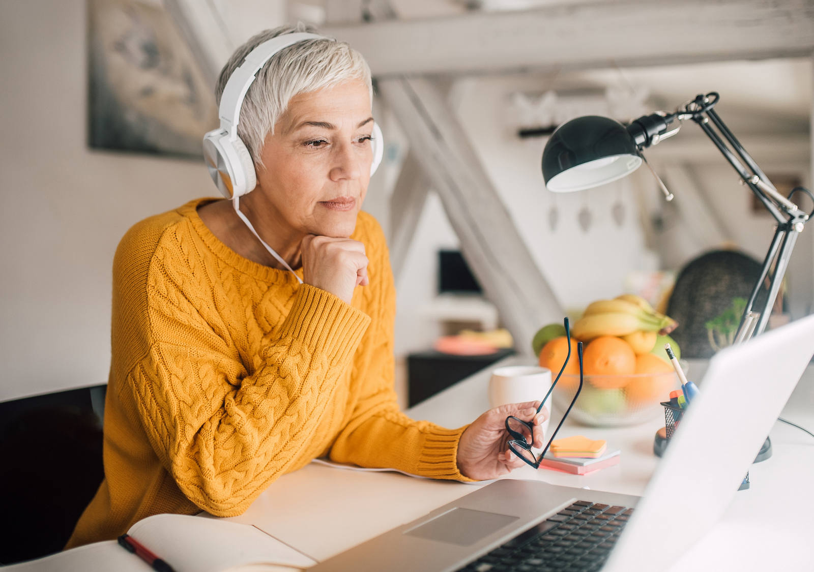 Una donna anziana lavora con le cuffie al suo laptop.