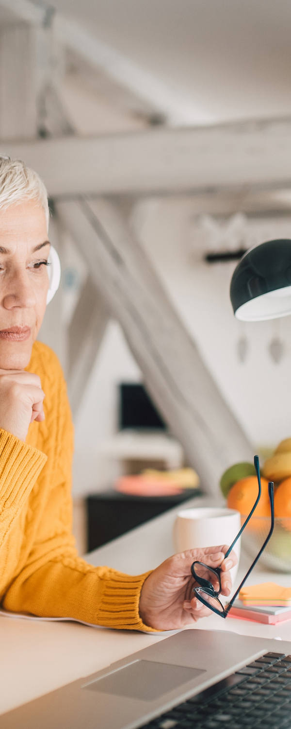 Ältere Frau arbeitet mit Kopfhörern an ihrem Laptop.