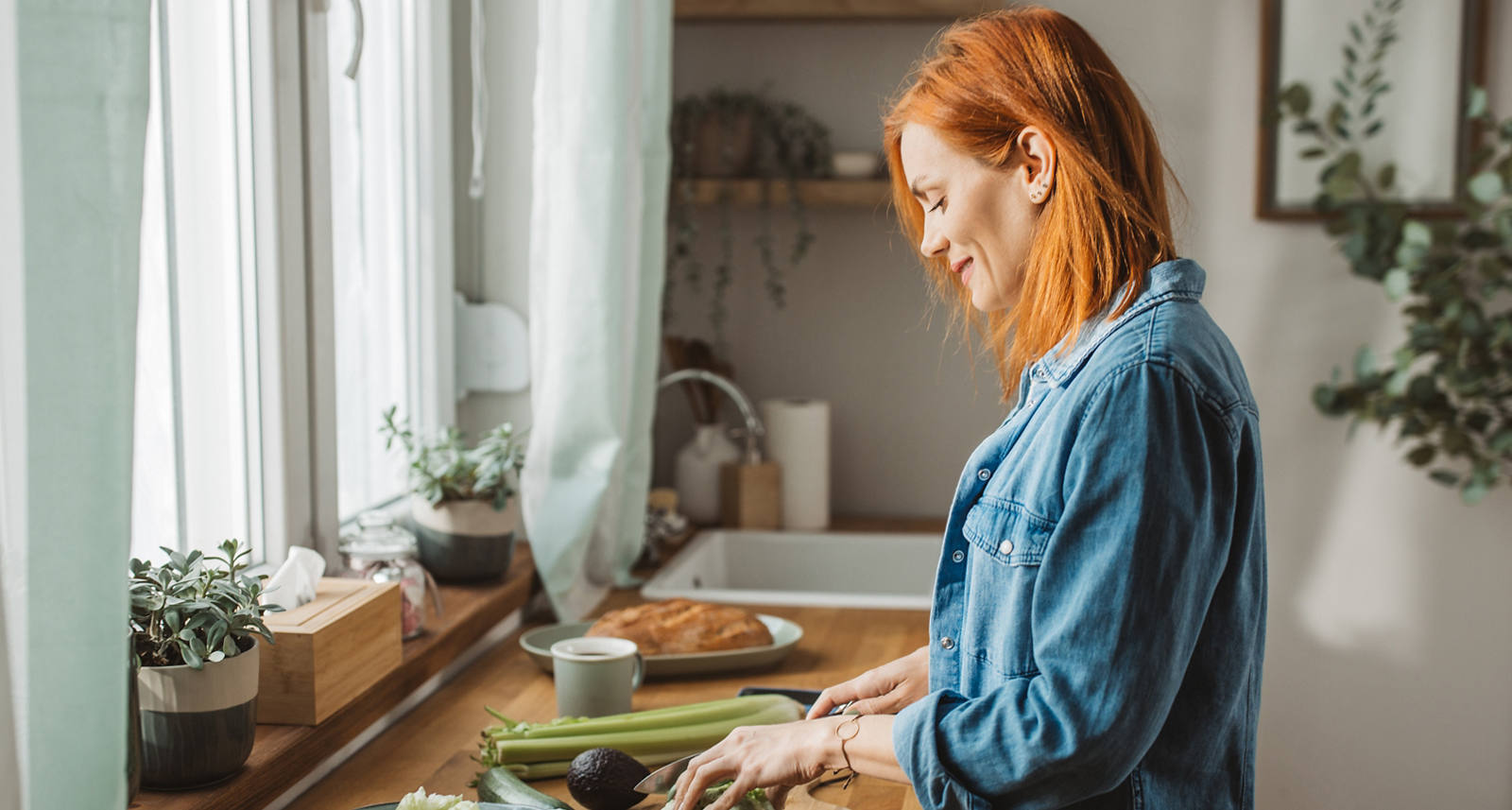 Eine Frau steht in der sonnigen Küche und schneidet Gemüse für einen Salat.