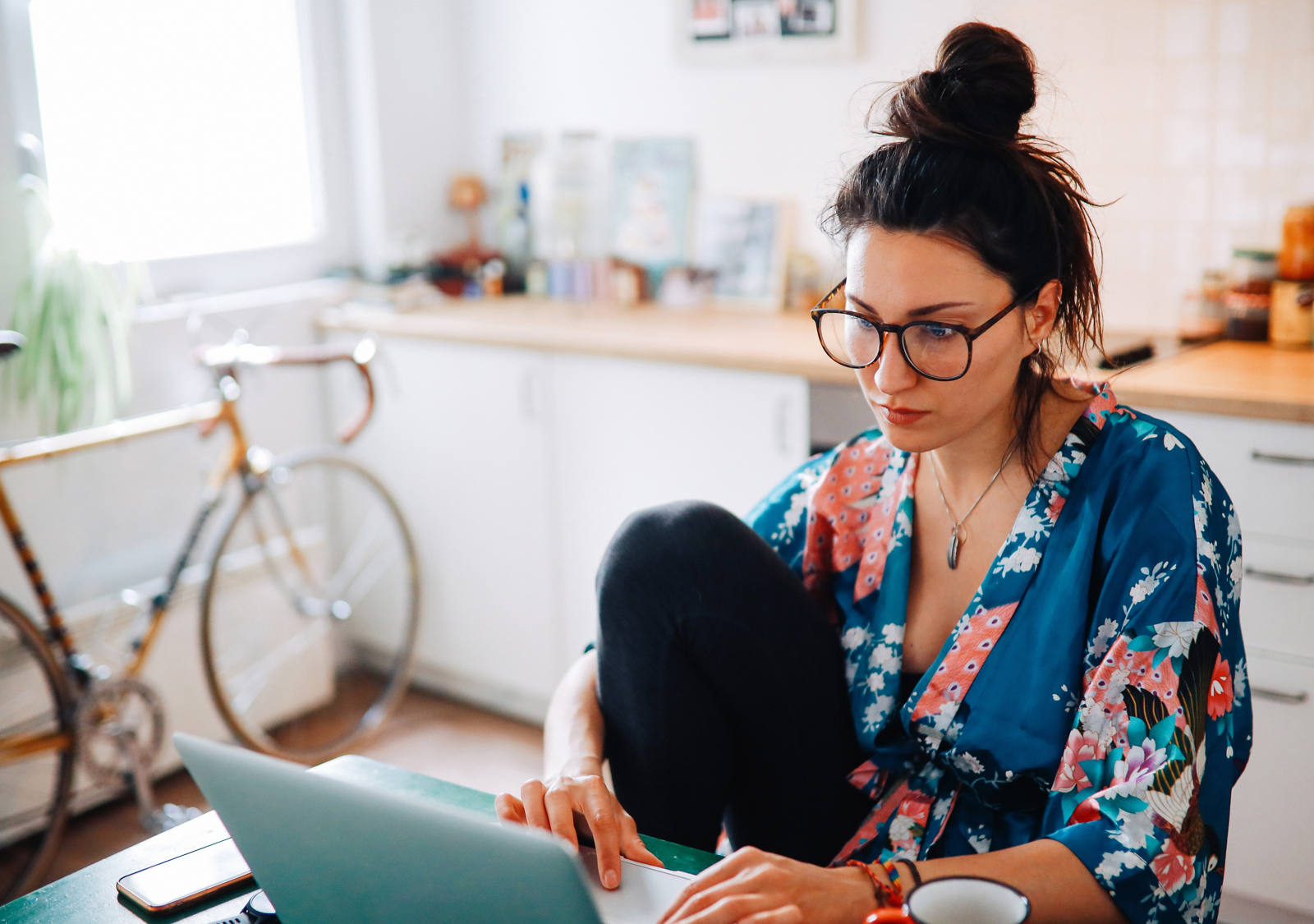 Une femme est assise à la table de la cuisine et travaille sur un ordinateur portable