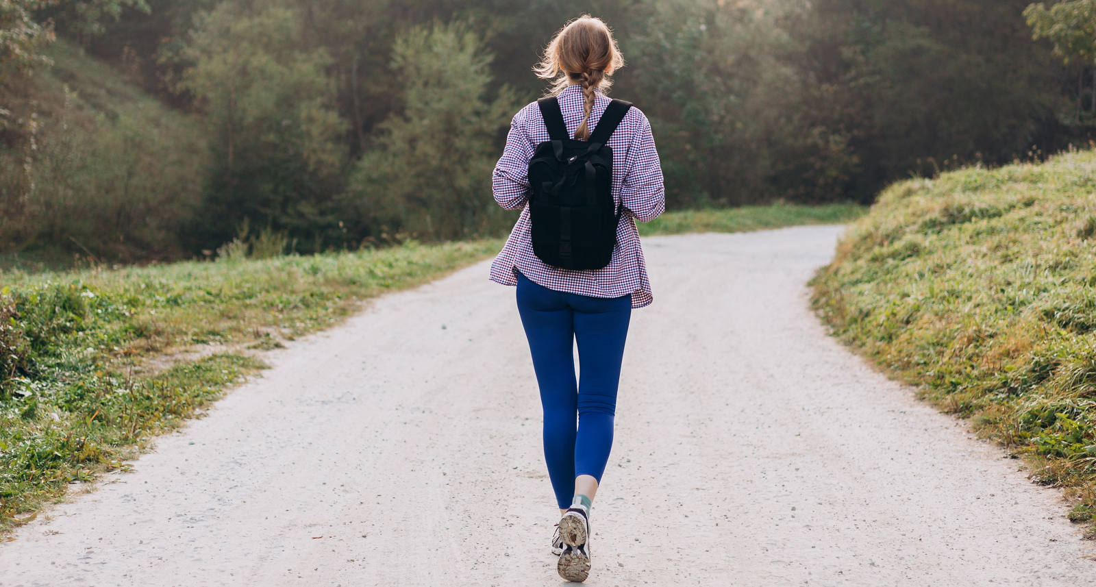 Eine Frau mit Rucksack wandert draussen in der Natur einen Weg entlang.