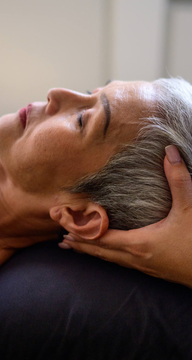  A woman lies on the massage table with her eyes closed and receives cranio-sacral therapy