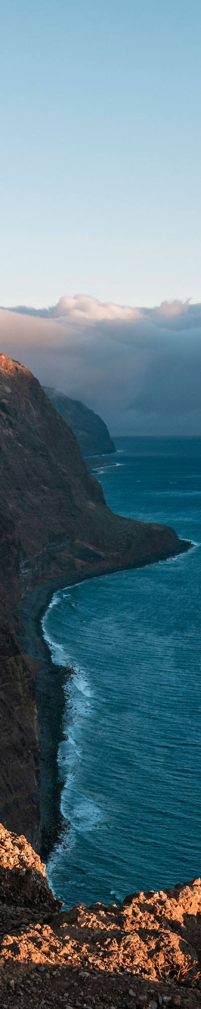 Young woman with backpack looking down from cliffs on sea bay