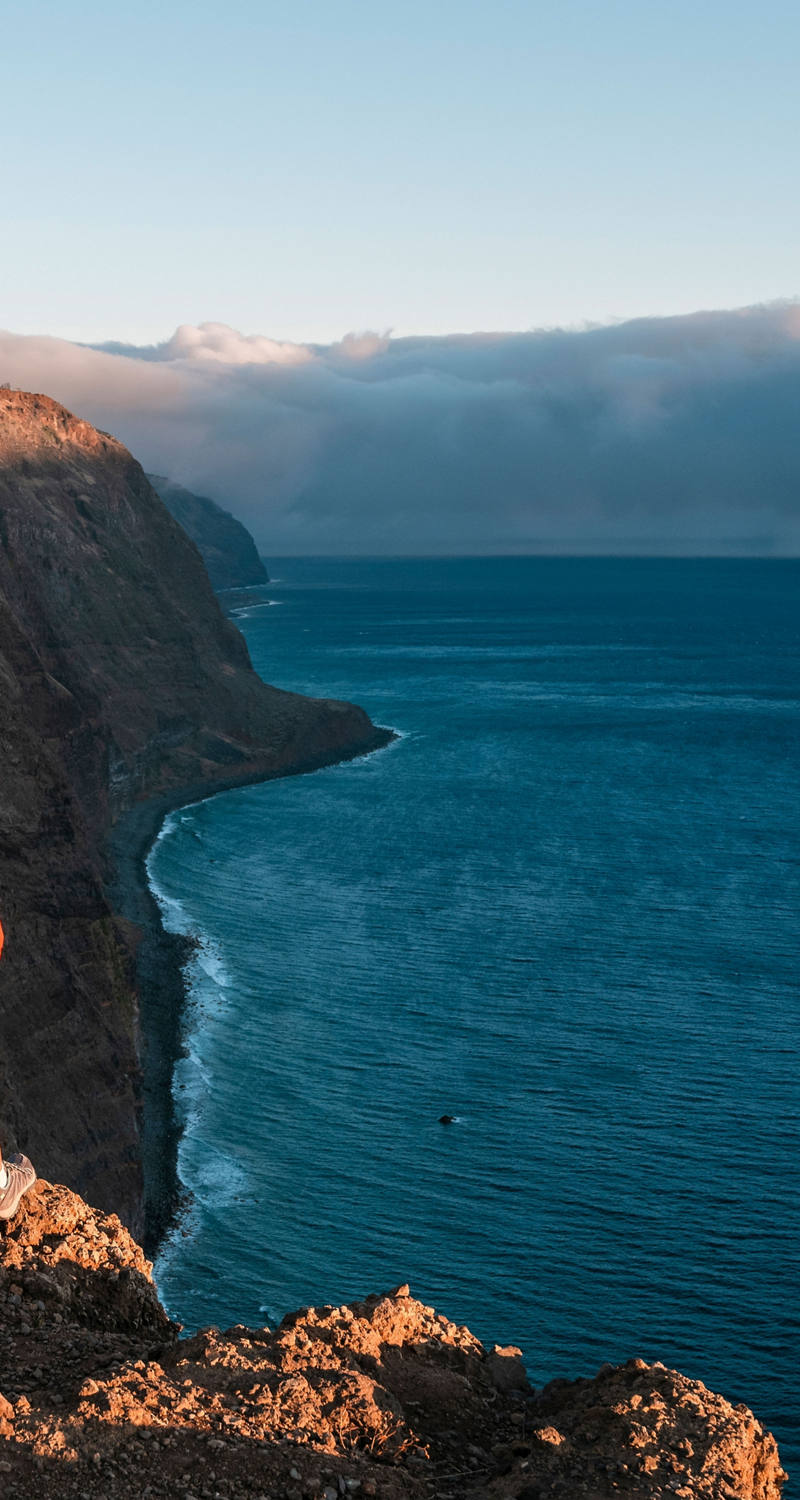 Young woman with backpack looking down from cliffs on sea bay
