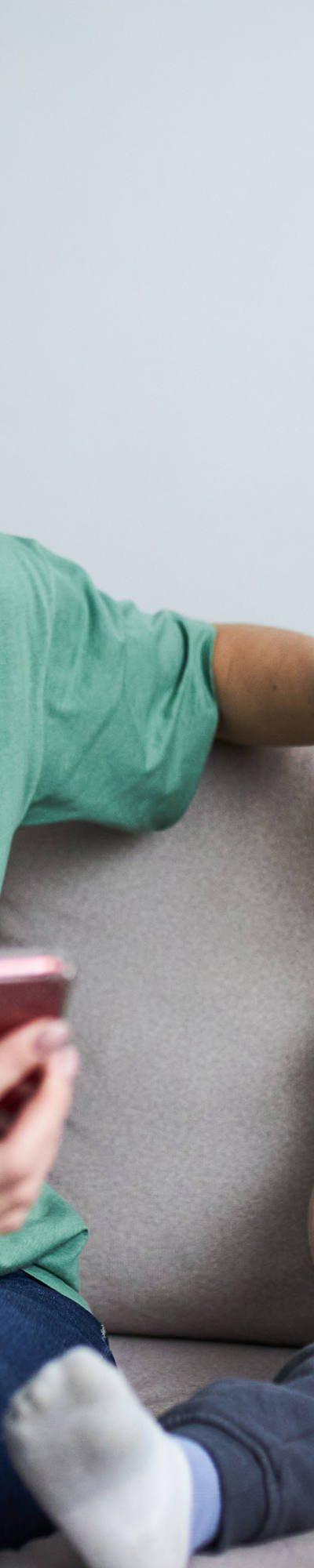 Mutter hält Hand an die warme Stirn von Kleinkind und schaut auf Smartphone.