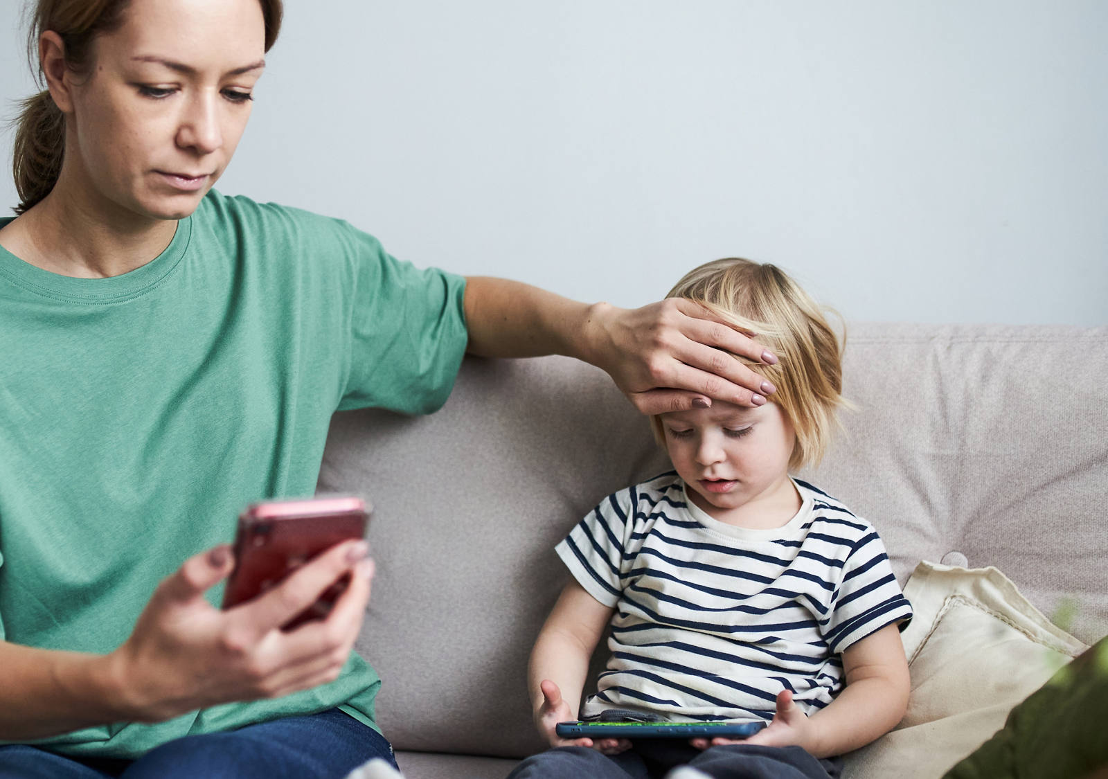 La mamma tiene la mano sulla fronte calda del bambino e guarda lo smartphone.