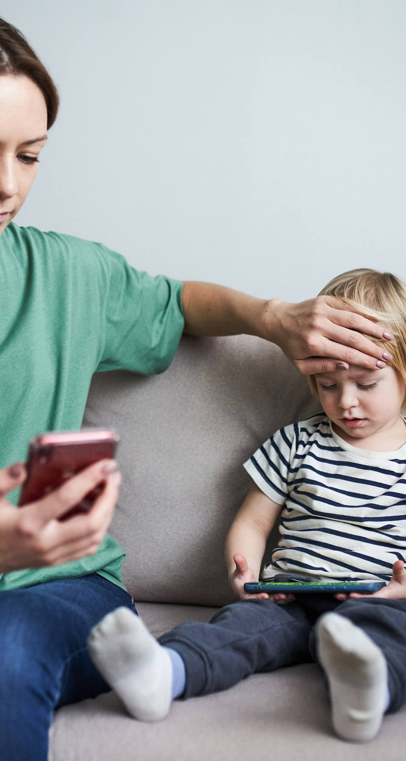 La mamma tiene la mano sulla fronte calda del bambino e guarda lo smartphone.