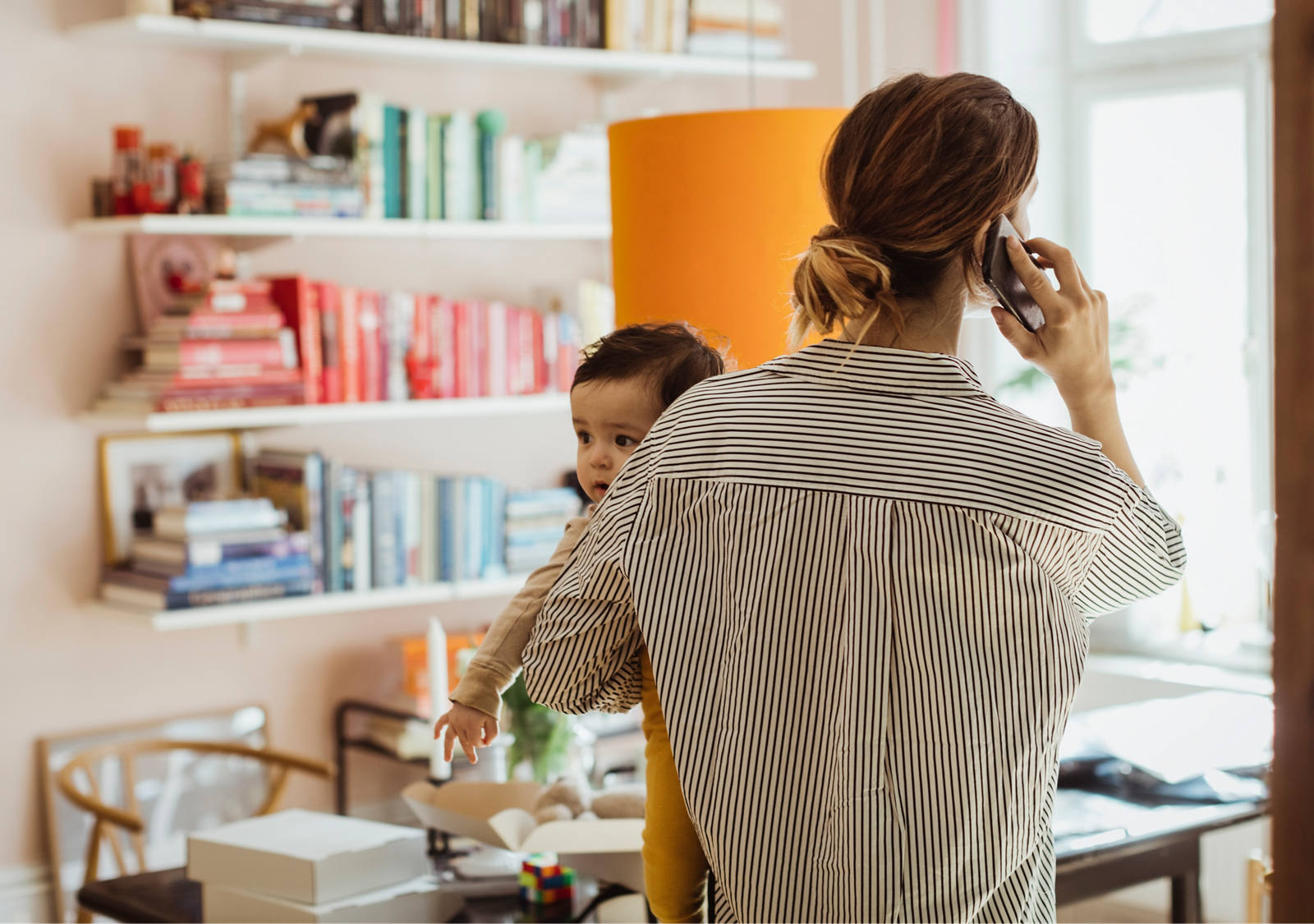 Mutter mit Kleinkind auf dem Arm steht in ihrem Büro und telefoniert.