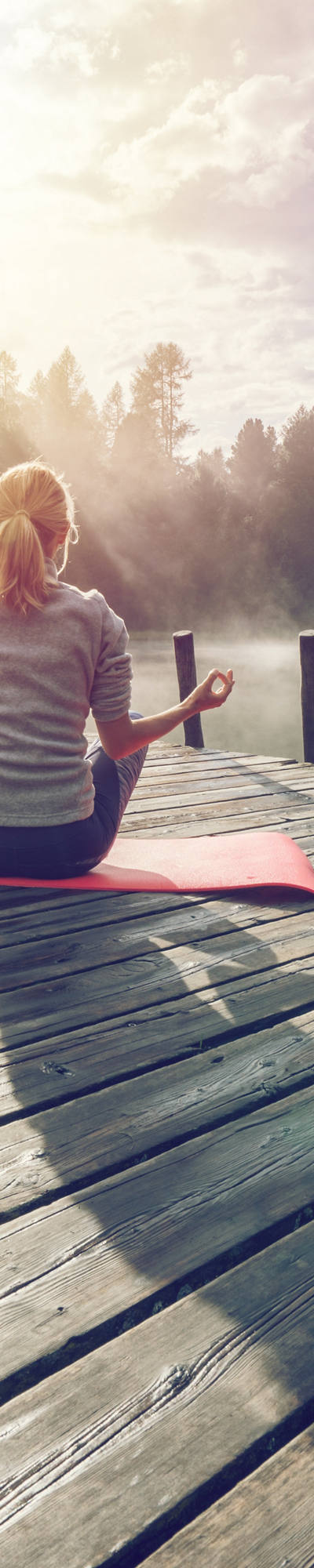 Frau meditiert auf roter Yogamatte auf einem Holzsteg am See.