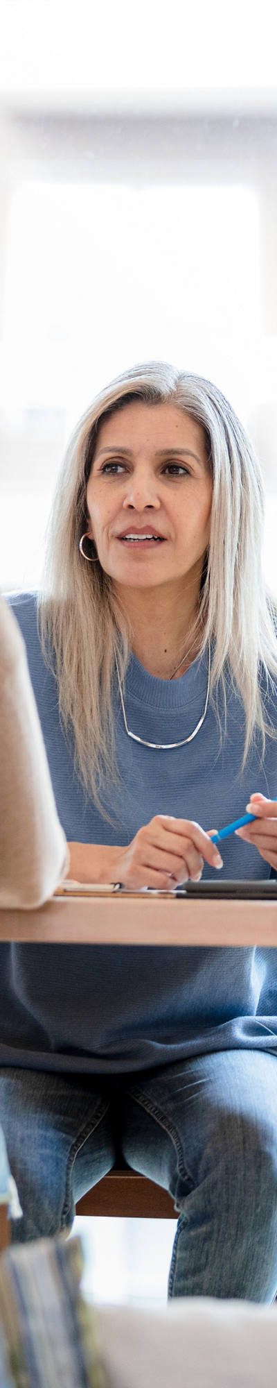 Una dottoressa è seduta intorno al tavolo in una stanza e ha una paziente in cura. Essi conducono una conversazione.