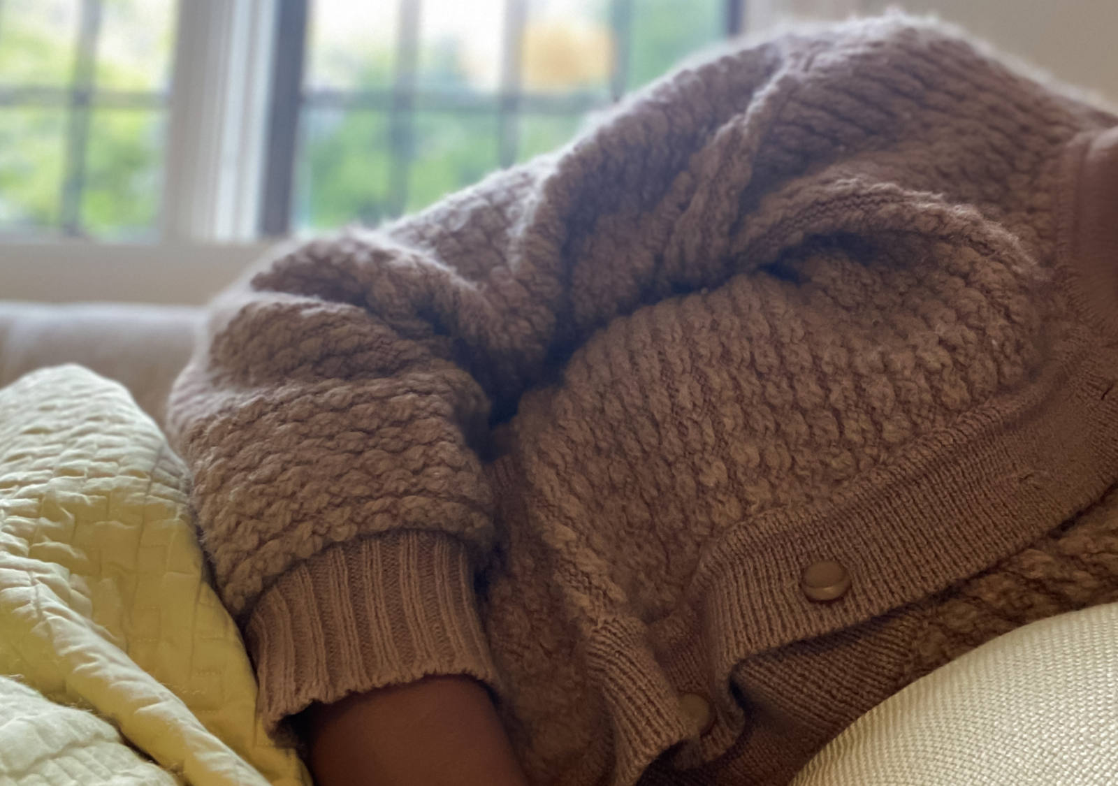 Une femme en pull brun est allongée dans un lit de réfection.