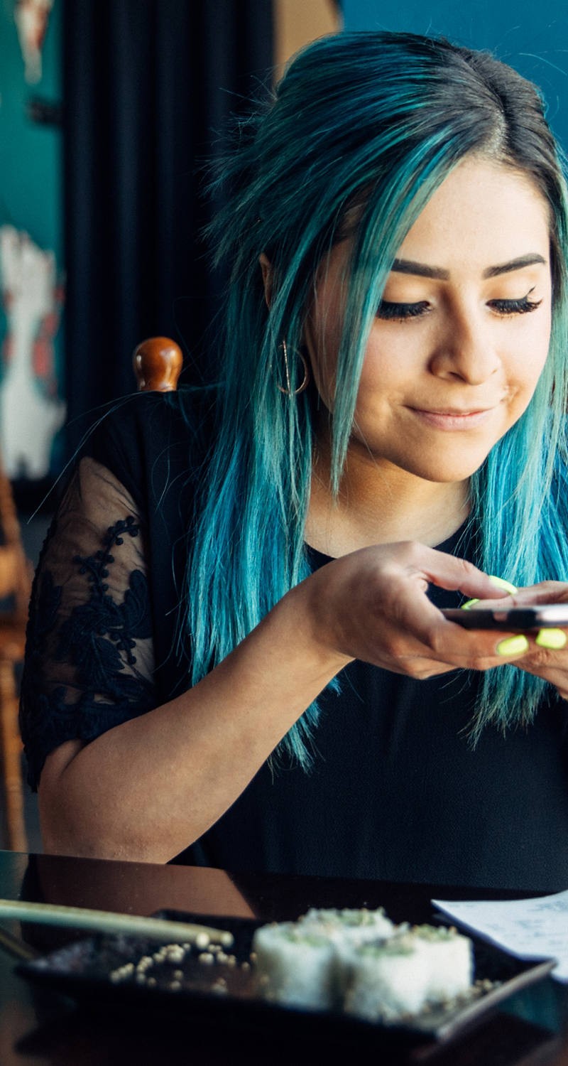 Junge Frau mit blauen Haaren fotografiert mit Smartphone eine Rechnung