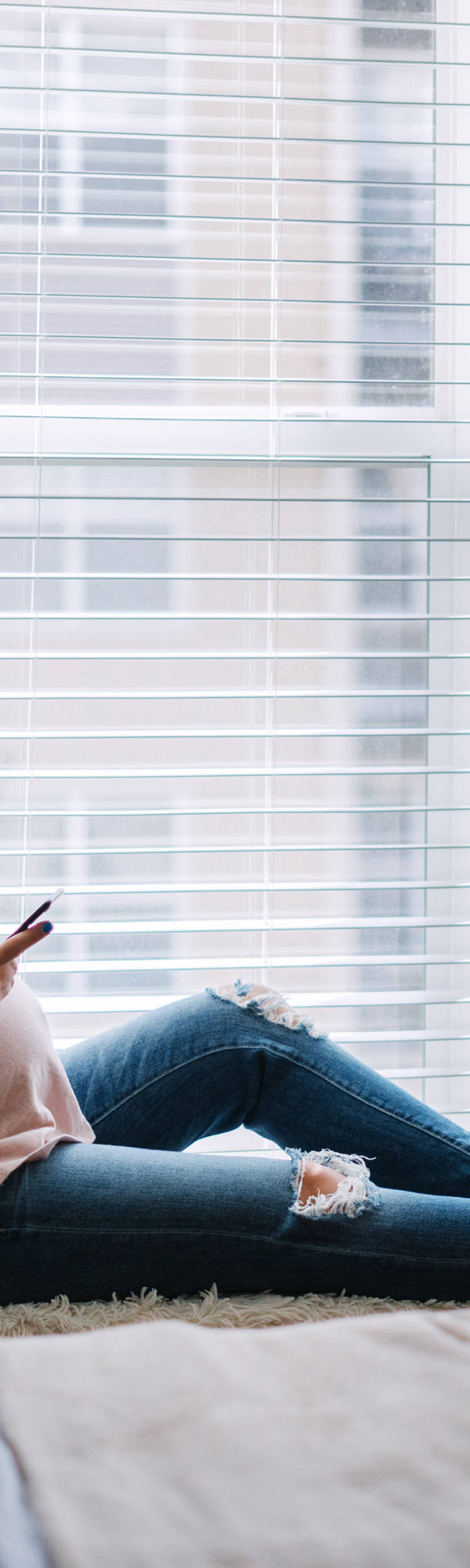 Pregnant woman drinking tea on windowsill and scrolling on smartphone