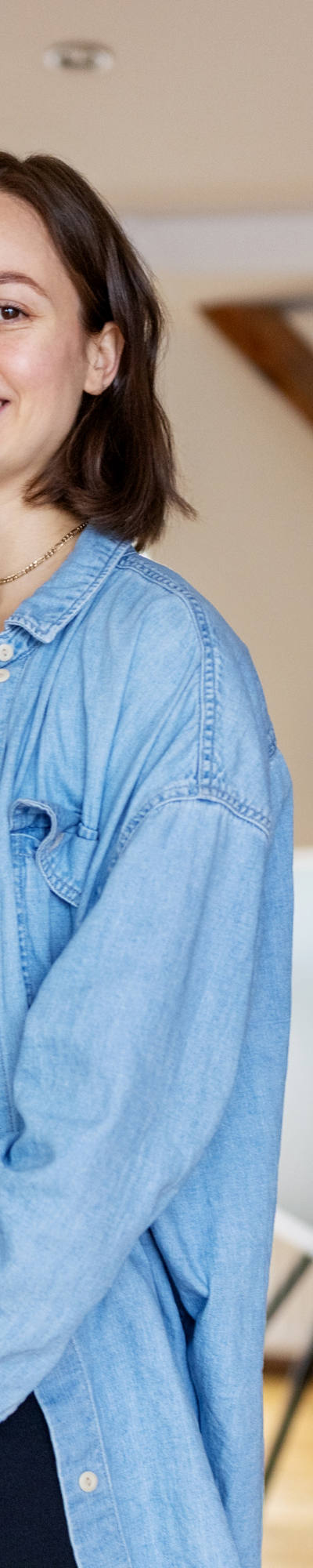 Schwangere Frau steht im Wohnzimmer und zeigt ihren Babybauch und strahlt in die Kamera.