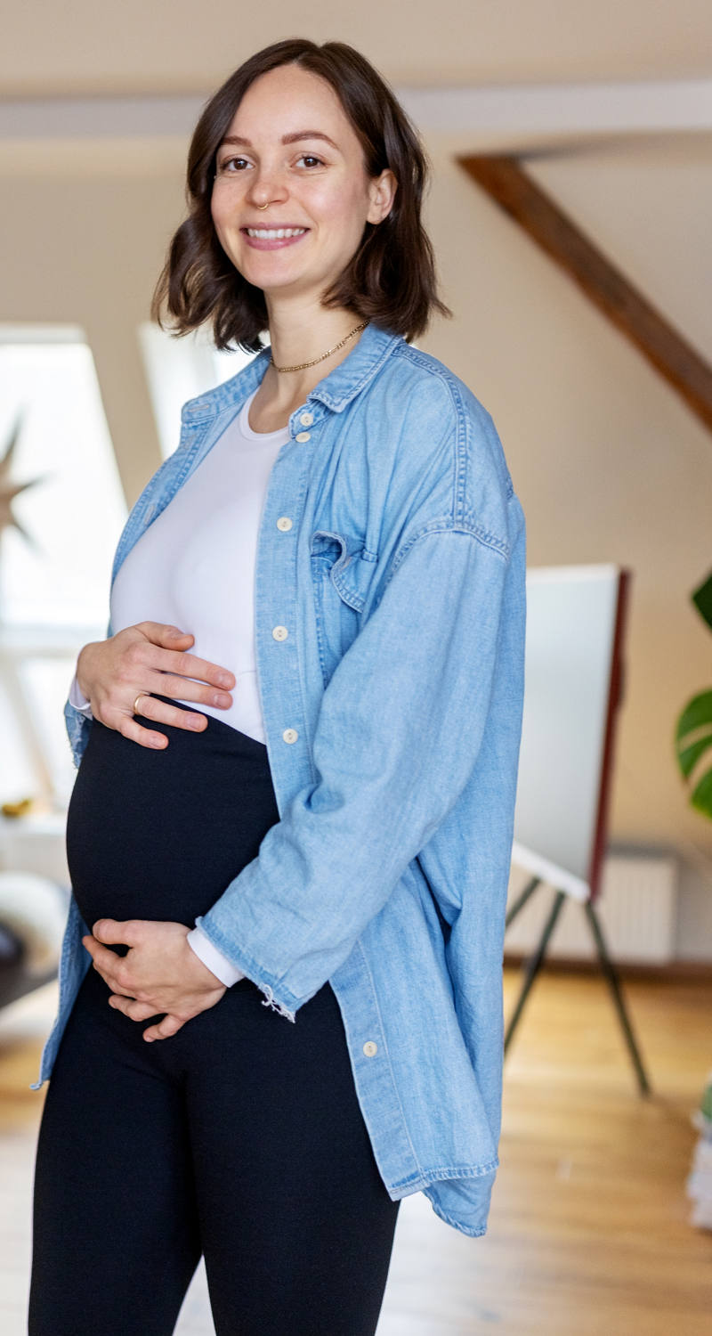 Una donna incinta è in salotto e mostra il suo pancione e si illumina verso la telecamera.